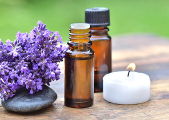 bottles of essential oil with lavender flower arranged on a wooden table in garden with candle