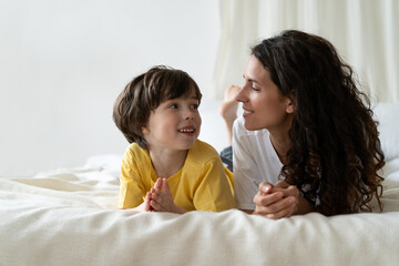 Young single parent mother enjoy spending weekend morning lying on bed with preschool son of 5,...