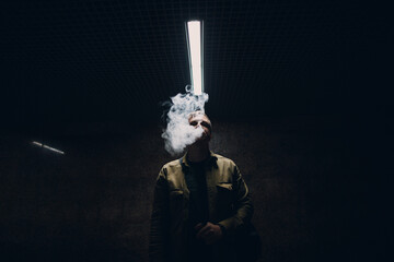 Portrait of young caucasian man smoking e-cigarette in dark with line light.