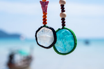 Close-up colorful handmade keychains made of crystal stones with blue sea background. Popular as a...