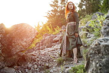 Beautiful red-haired girl-archer of Middle Ages among rocks. Fantastic concept