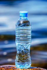 A bottle of drinking water stands on a stone on the seashore
