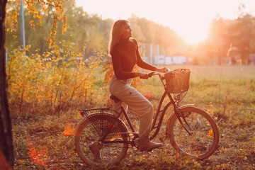Obraz premium Happy active young woman riding vintage bicycle in autumn park at sunset.
