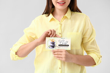 Young woman with gift certificate for massage on light background