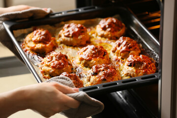 Woman taking baking tray with minced meat boats, mushrooms and cheese out of oven