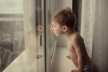 Little kid is looking out the window. Image with selective focus and toning