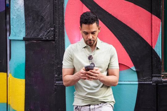 Young Latino Young Man Texting, Checking Social Networks, Chatting On His Smart Phone On Colorful Background. 