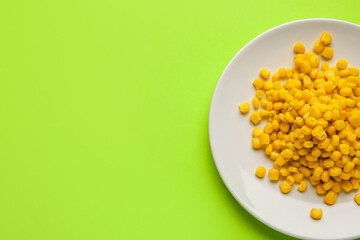 Plate with corn kernels on color background