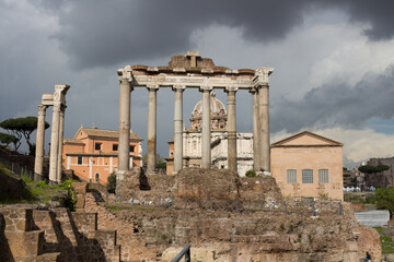 Roman forum in the sun against a dark, clouded sky. Ancient architecture and cityscape of historical Rome.