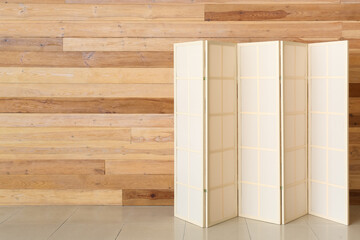Stylish folding screen near wooden wall