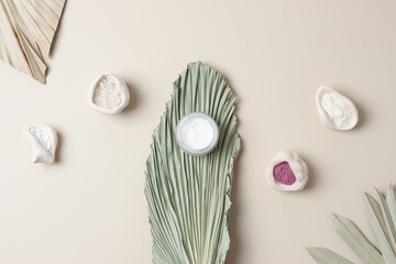 Jar of cosmetic cream and mask with palm leaf on pastel beige background. Flat lay