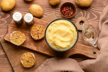 Bowl of tasty mashed potatoes with garlic and vegetables on wooden background