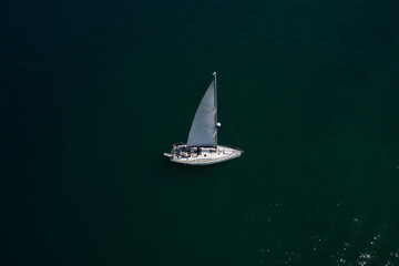 Large white boat with sails on blue water aerial view. Lonely sailboat on the water top view. Boat with sails, blue water with high altitude. Sailboat on Lake Garda, Italy.