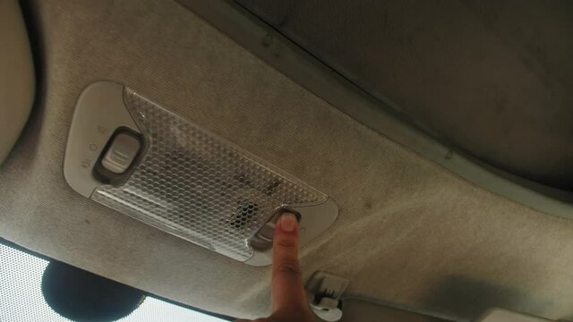 Person presses the button to open the sunroof in the car, close up.