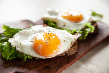 Closeup yummy toasts with fried eggs and lettuce leaves for breakfast placed on wooden board