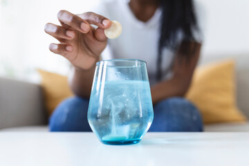 Closeup of a young woman dropping an effervescent antacid in a glass of water. young woman hardly...