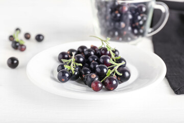 Plate with ripe black currant on light wooden background