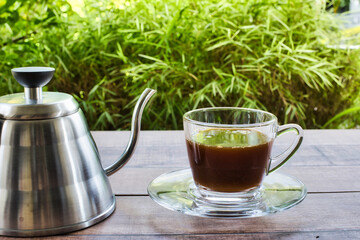 A glass of coffee on wooden table over blurred tree with sun lighting. Image vintage photo.