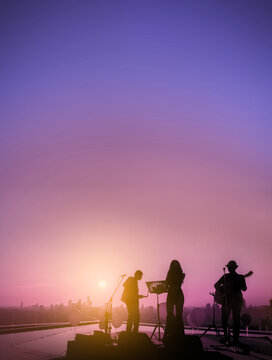 Silhouetted trio musician with sunset sky and sunlight flare effect background.