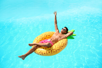Handsome man with inflatable ring in swimming pool