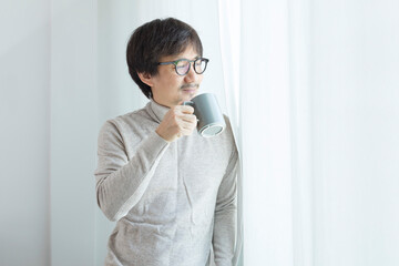 Middle-aged Asian man wear turtle neck drink coffee and using ideas standing by the window.