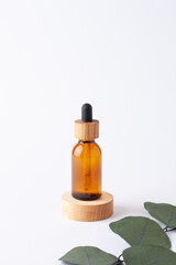 Cosmetic bottle with a wooden podium with eucalyptus on white background. Close up, copy space