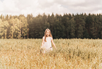 A little blonde girl walks through a golden field in the summer. Concept of purity, growth, happiness