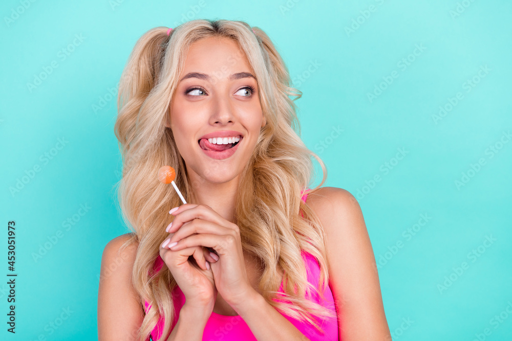 Sticker Photo of young girl happy positive smile hold lollipop sweet lick teeth tongue look empty space isolated over teal color background