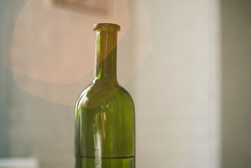 A vintage retro bottle made of green glass stands on the kitchen table. The sun is shining and lens flare enters the frame