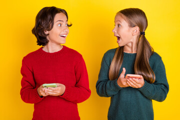 Photo portrait two children amazed using cellphones looking each at other isolated vivid yellow color background