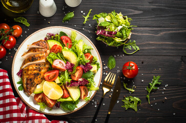 Healthy food concept. Grilled chicken with fresh salad. Top view at dark wooden table.