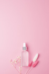 Cosmetic bottle with flowers on pink background. Flat lay, copy space