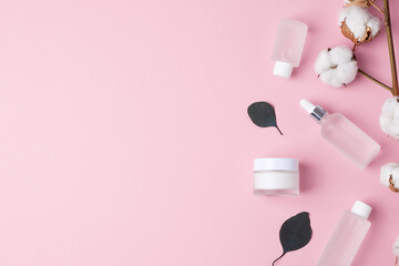 Cosmetic skin care products with flowers and eucalyptus on pink background. Flat lay, copy space