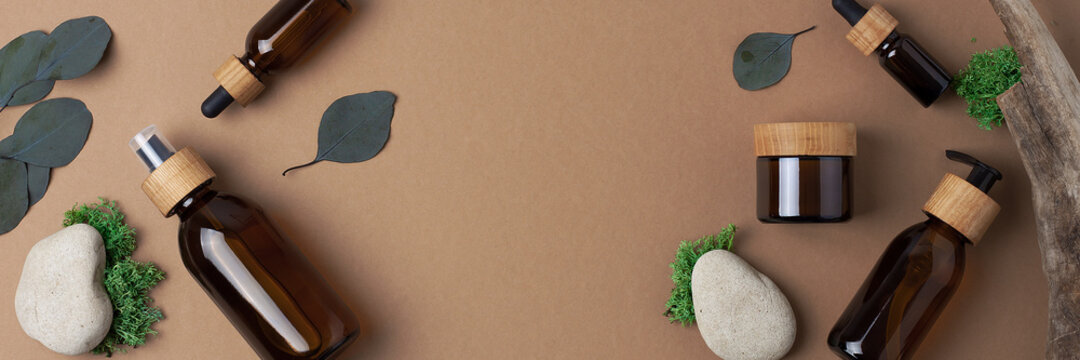 Cosmetic skin care products with eucalyptus and wood on brown background. Flat lay, copy space