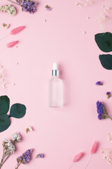 Cosmetic bottle with flowers and eucalyptus on pink background. Flat lay