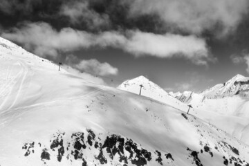 Off-piste slope and chair-lift on ski resort. Black and white toned landscape.