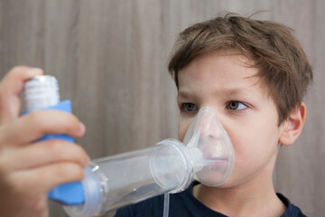 Child boy using medical spray for breath. Inhaler, spacer and mask. Side view