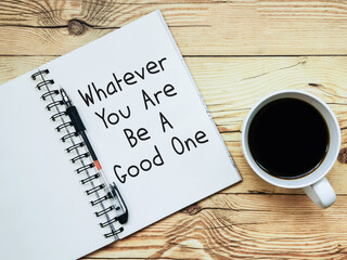 Open notebook with text "Whatever you are be a good one" and a cup  of coffee on wooden background.
