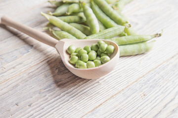 Wooden spoon with green peas and pods on a light wooden background. Ecological food