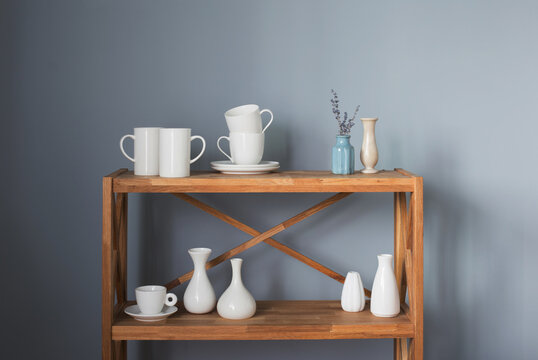 white cups and vases on wooden shelf on gray background
