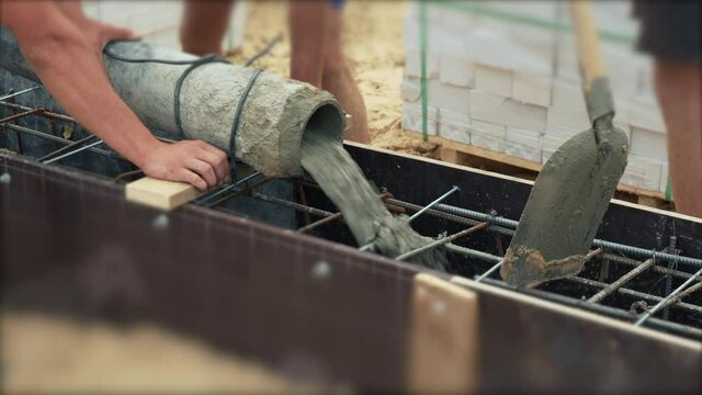 Pouring ready-mixed concrete in formwork with reinforcement. Wet cement pours to civil building foundation, close up.