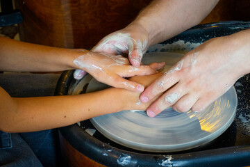 hands of a child and an adult on a potter's wheel in a pottery workshop, clay modeling, children's creativity under the supervision of adults