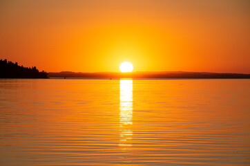 Tramonto sul lago Trasimeno in Umbria, con bellissime sfumature e colori arancio vivo e con  l'immagine al centro del cerchio infuocato sopra le colline al tramonto.