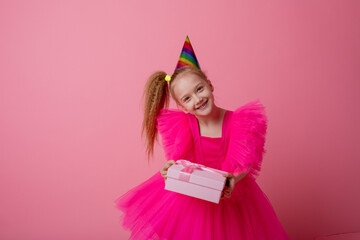 a little girl holds a gift on a pink background celebrating her birthday