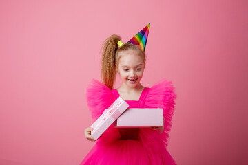 a little girl on a pink background opens a gift celebrating her birthday