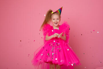 a little girl on a pink background blowing confetti celebrates her birthday