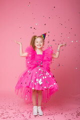 a little girl on a pink background catches confetti celebrates her birthday
