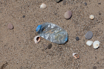 Crumpled single-use plastic bottle on the beach. Plastic garbage thrown by sea wave on shore. Concept - Pollution of world ocean by household waste
