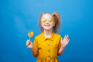 a little girl in sunglasses holds a lollipop on a blue background