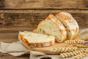 Freshly baked bread with wheat ears, fragrant pieces on a cutting board